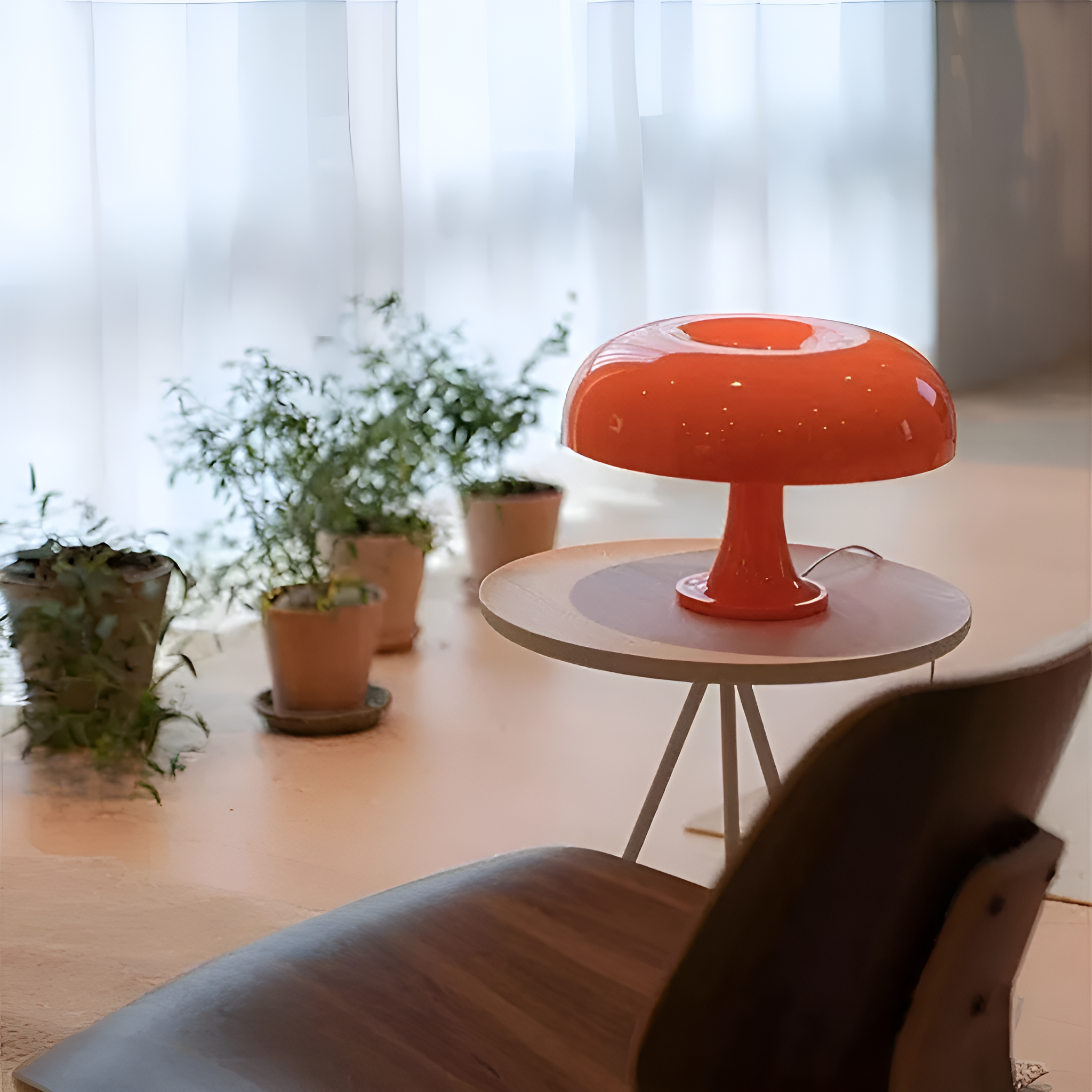 Eine orangefarbene pilzförmige Lampe auf einem kleinen Tisch, in der Nähe von Pflanzen und einem Stuhl.