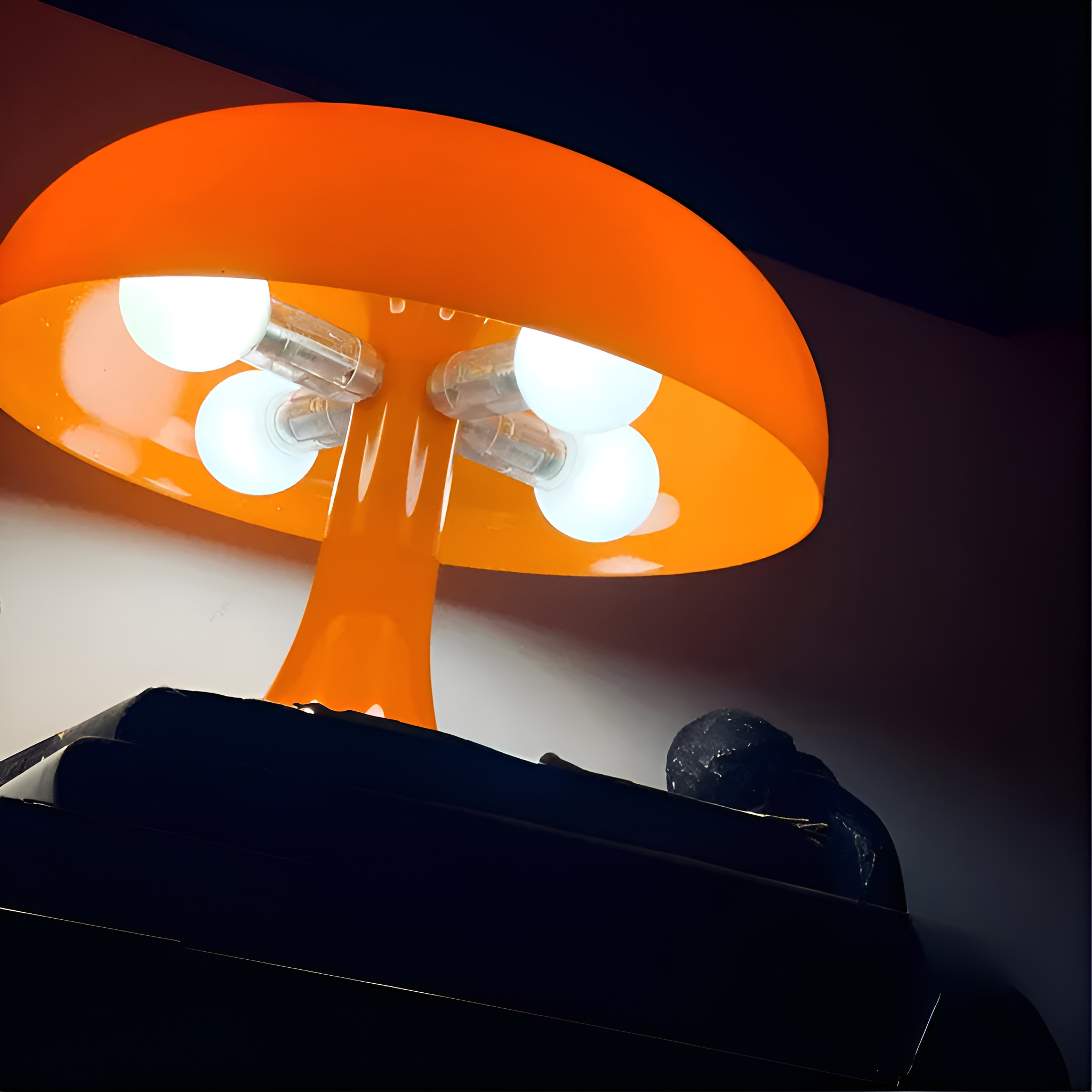 Orangefarbene pilzförmige Lampe mit vier Glühbirnen, auf dunklem Grund.