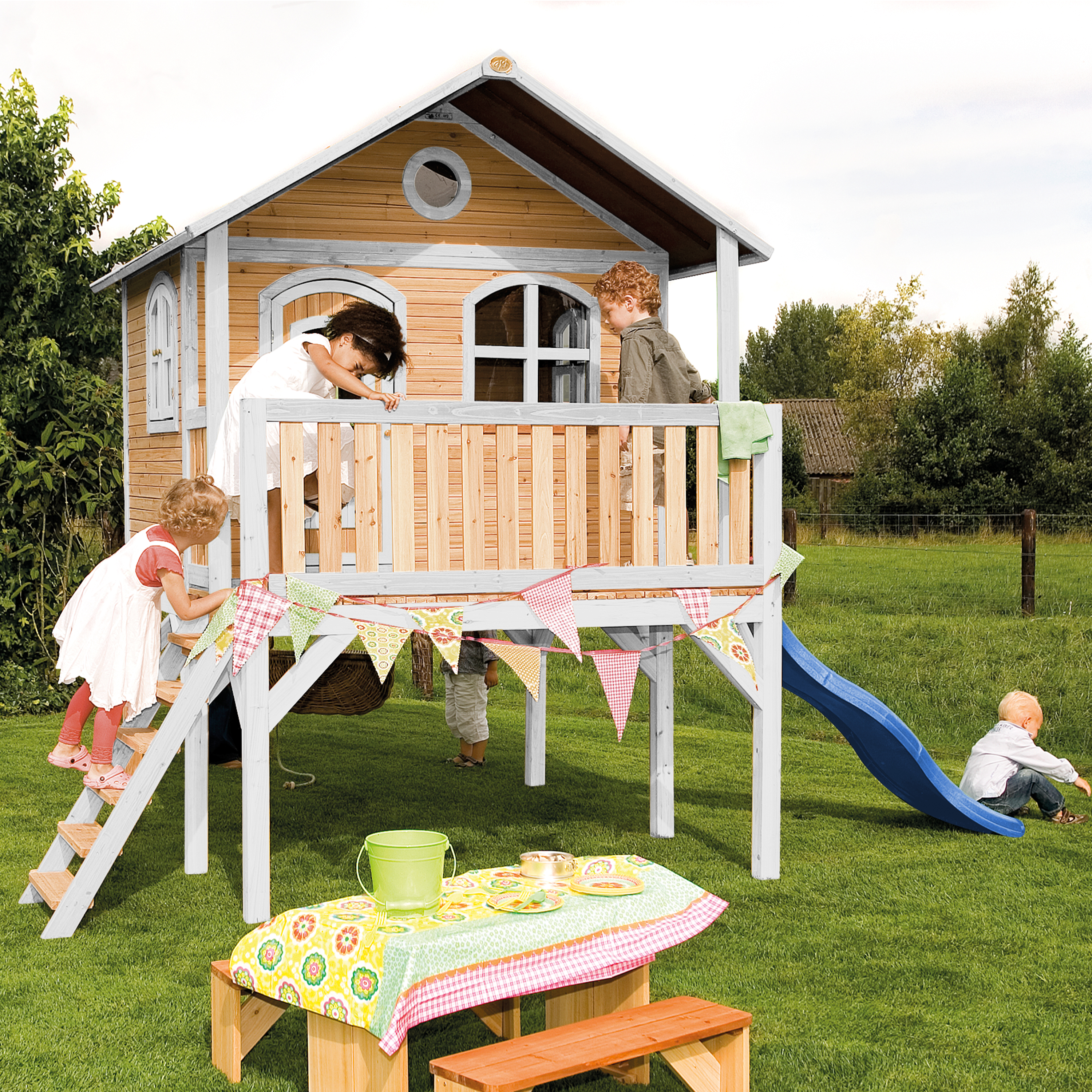 Kinder spielen auf einem Holzspielhaus mit Rutsche und Bank.