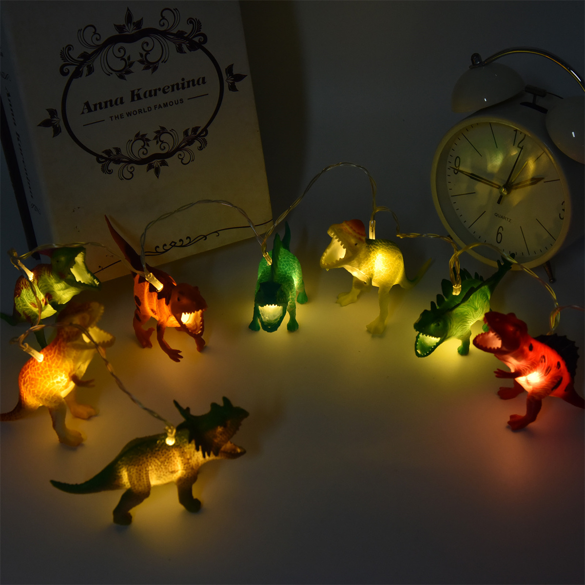 Eine Lichterkette in Dinosaurierform, im Hintergrund ein Buch und eine Uhr, bei Nacht.
