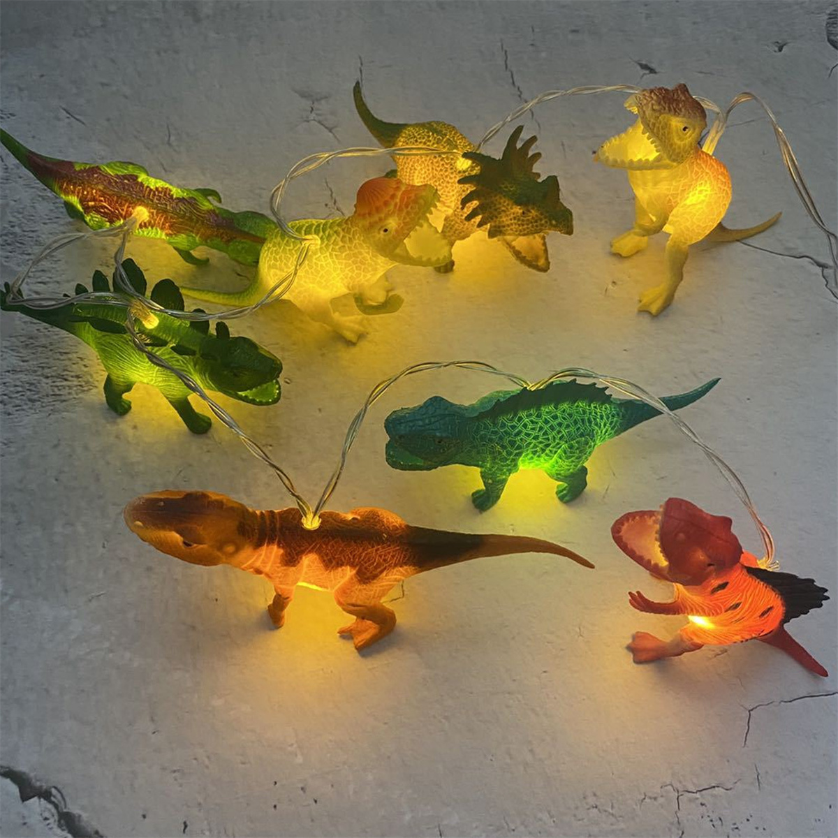 Lichterkette mit Dinosaurier-Formen, verschiedene Farben. Auf strukturierter Oberfläche.