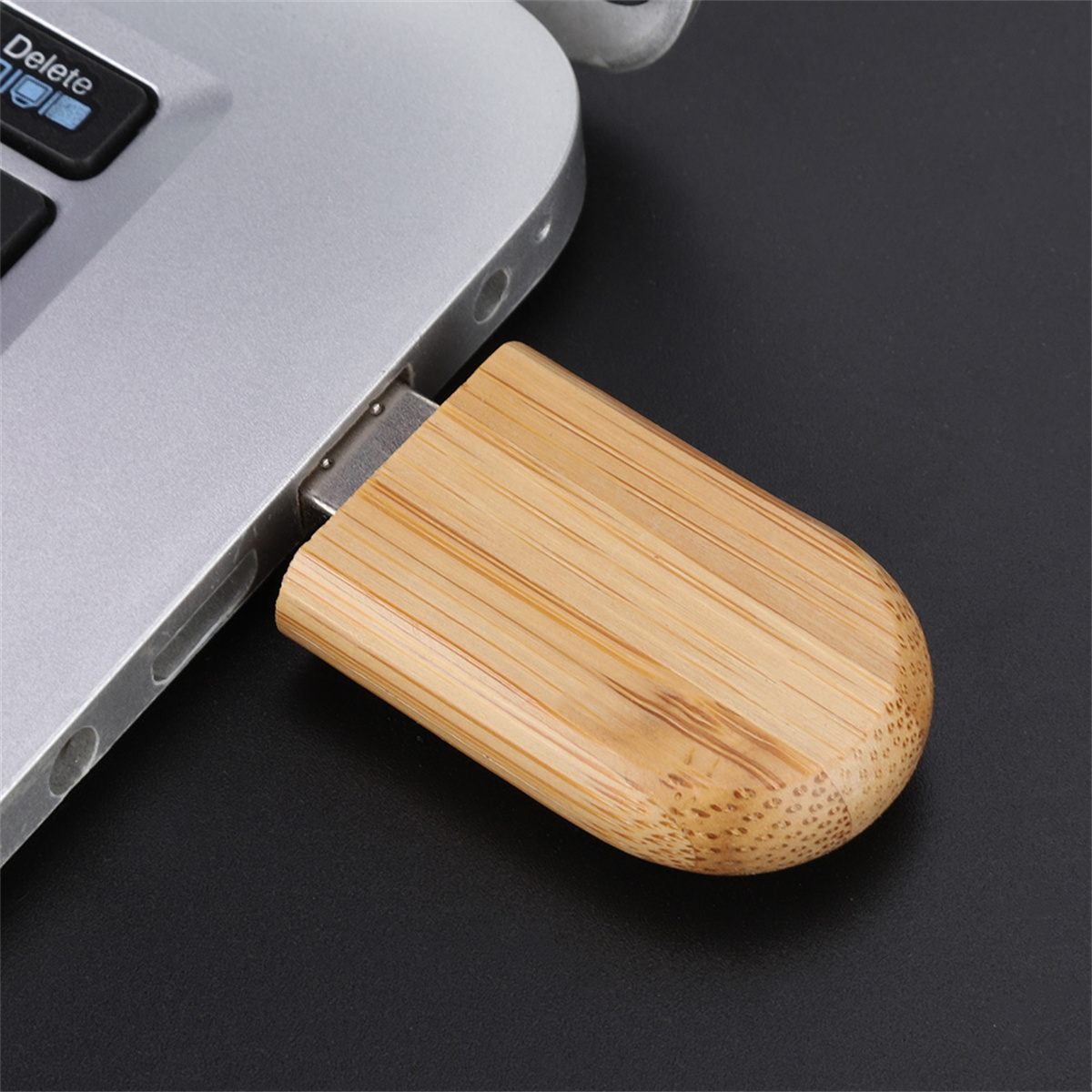 Ein hölzerner USB-Stick, der in einen Laptop gesteckt ist. Der Stick hat Holzmaserung, der Laptop ist silber.