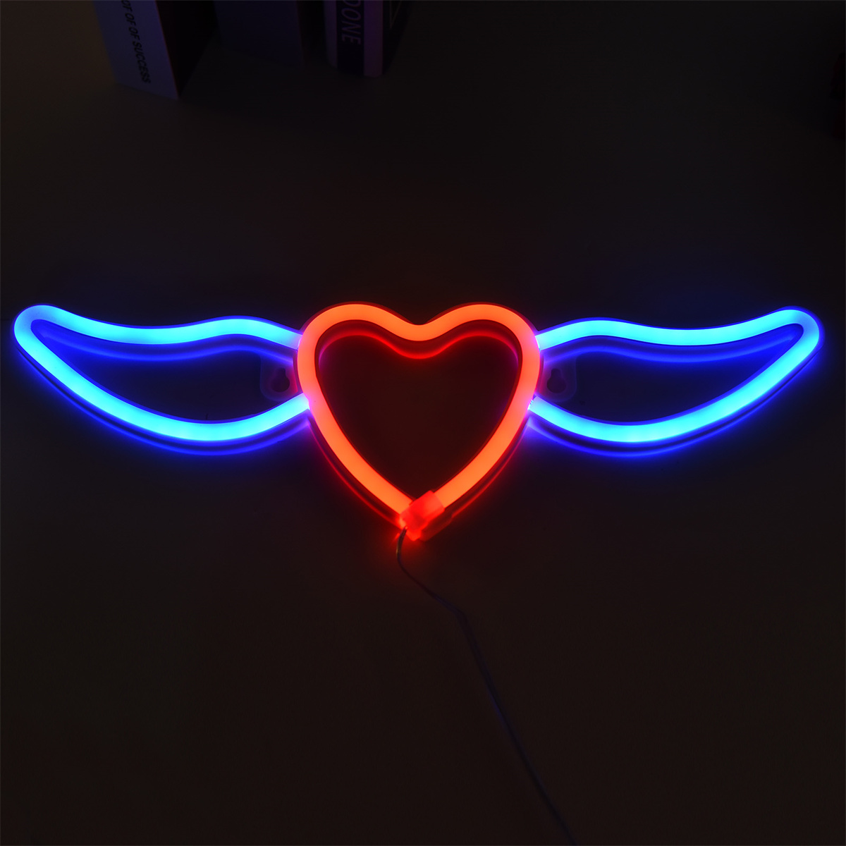 Neon-Herz mit Flügeln in Blau und Rot, auf dunkler Oberfläche montiert.