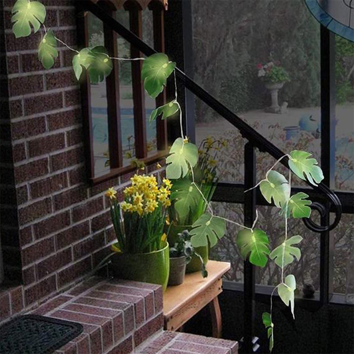 Eine Backsteintreppe mit einer blattförmigen Lichtgirlande. Gelbe Blumen stehen in Töpfen.