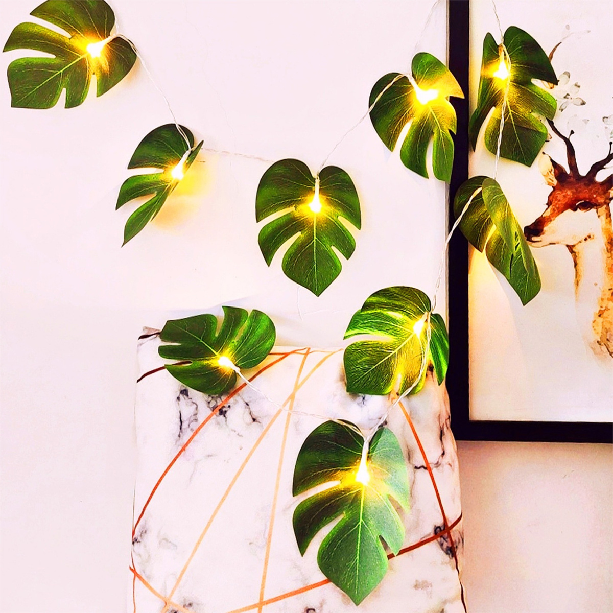 Grüne blattförmige Lichterketten an einer weißen Wand mit Kissen und Gemälde im Hintergrund.