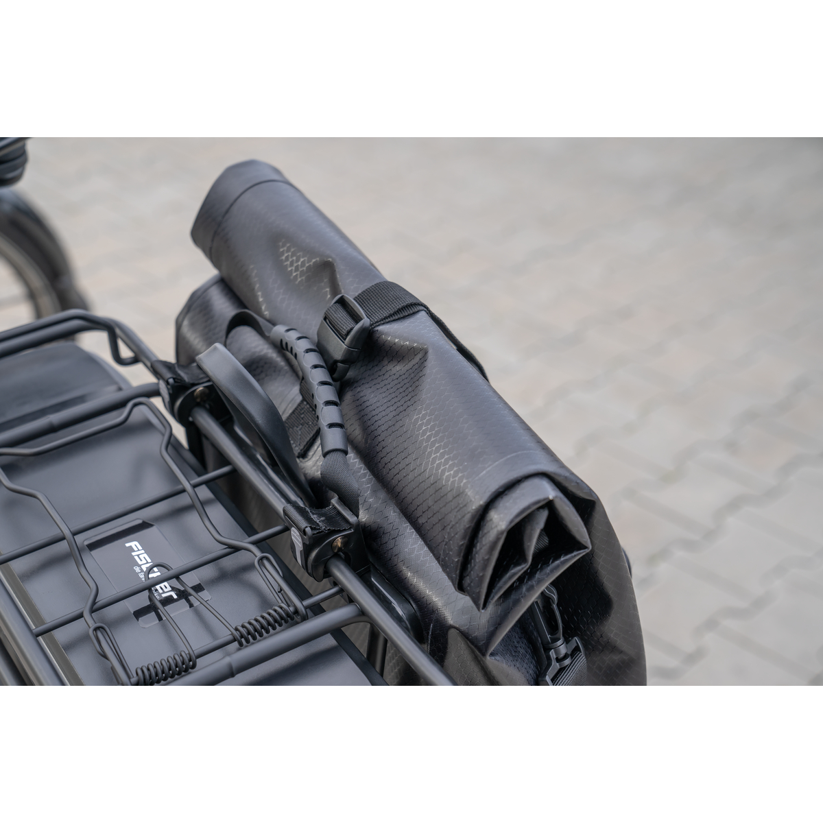 Eine schwarze Fahrradtasche ist am Heckträger eines Fahrrads befestigt. Die Tasche ist aufgerollt und gesichert.