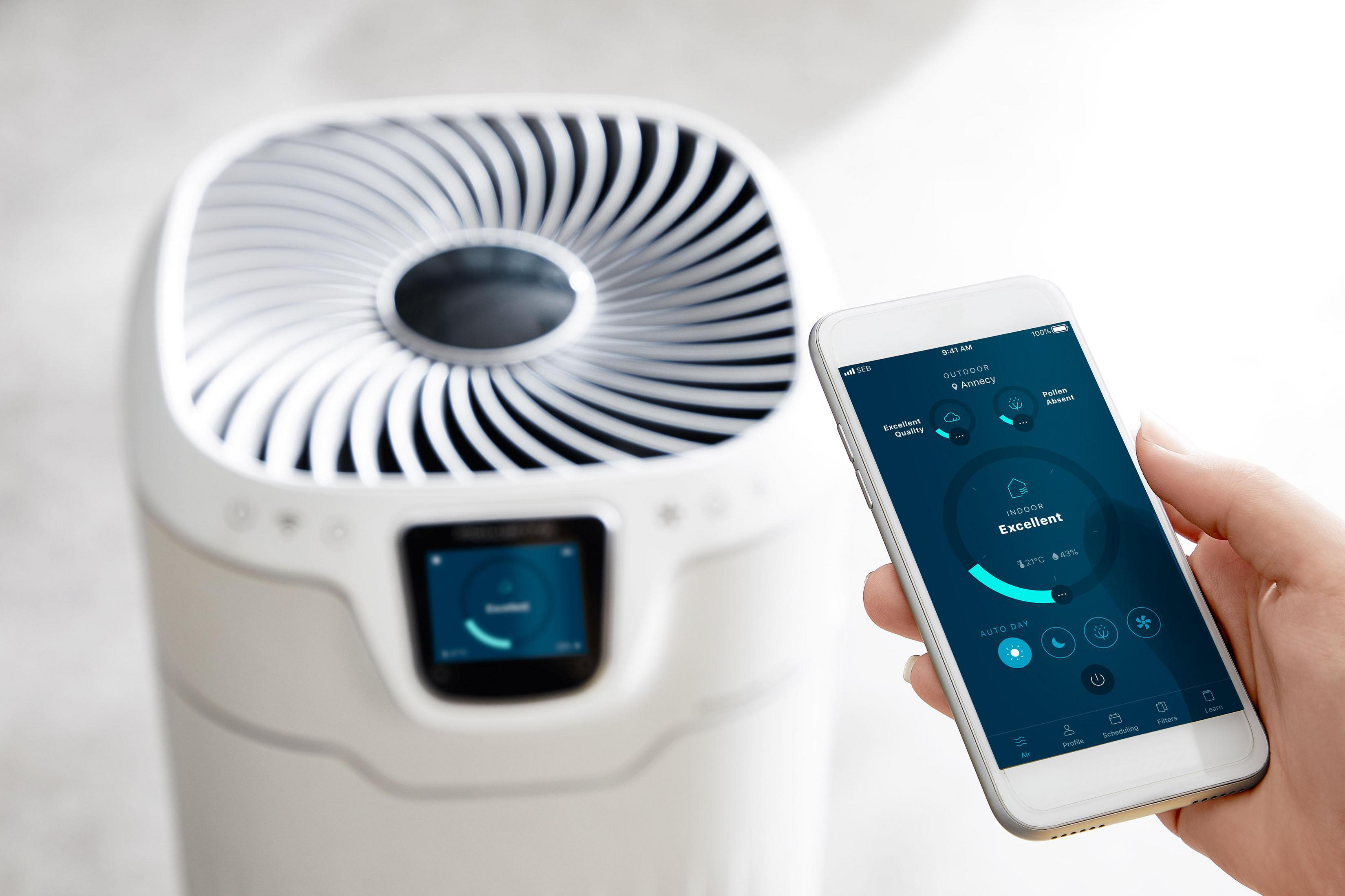Un purificatore d'aria bianco con uno smartphone che mostra la qualità dell'aria e una mano.