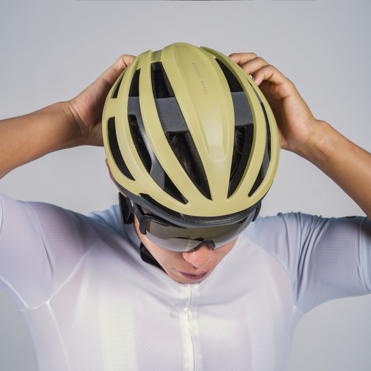 Person trägt einen gelben Fahrradhelm und eine Sonnenbrille. Grauer Hintergrund.