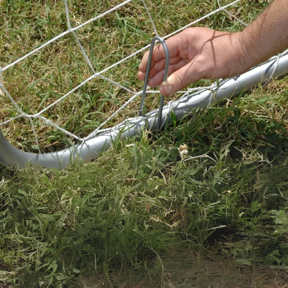Une main attache une attache métallique à un filet de but de football sur un champ herbeux.