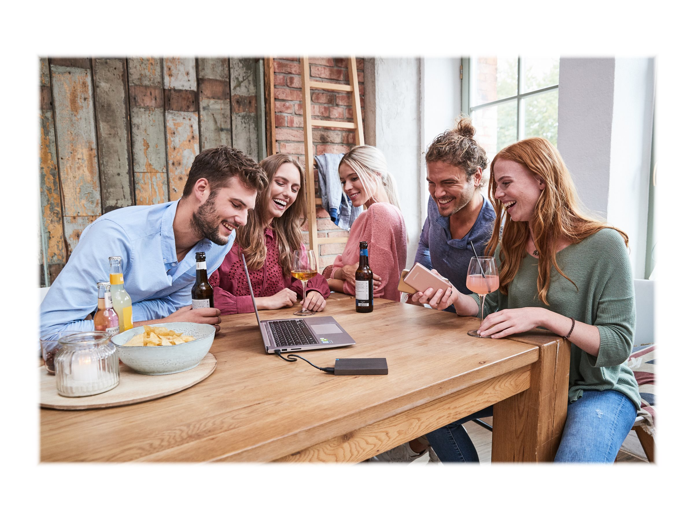 Grupa osób wokół drewnianego stołu z laptopem, napojami i przekąskami.