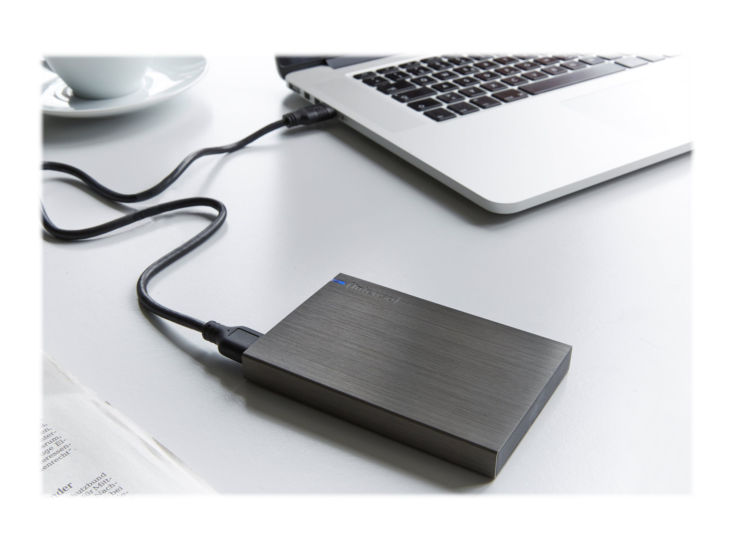 Srebrny laptop jest podłączony do ciemnoszarego dysku twardego na białej powierzchni.