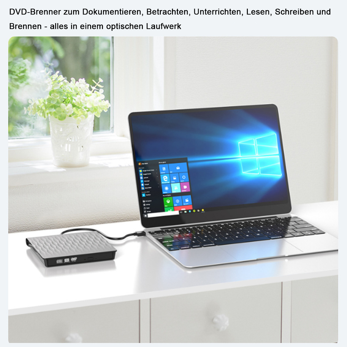 Laptop mit DVD-Player, weißem Tisch und grüner Pflanze in einer Vase am Fenster.