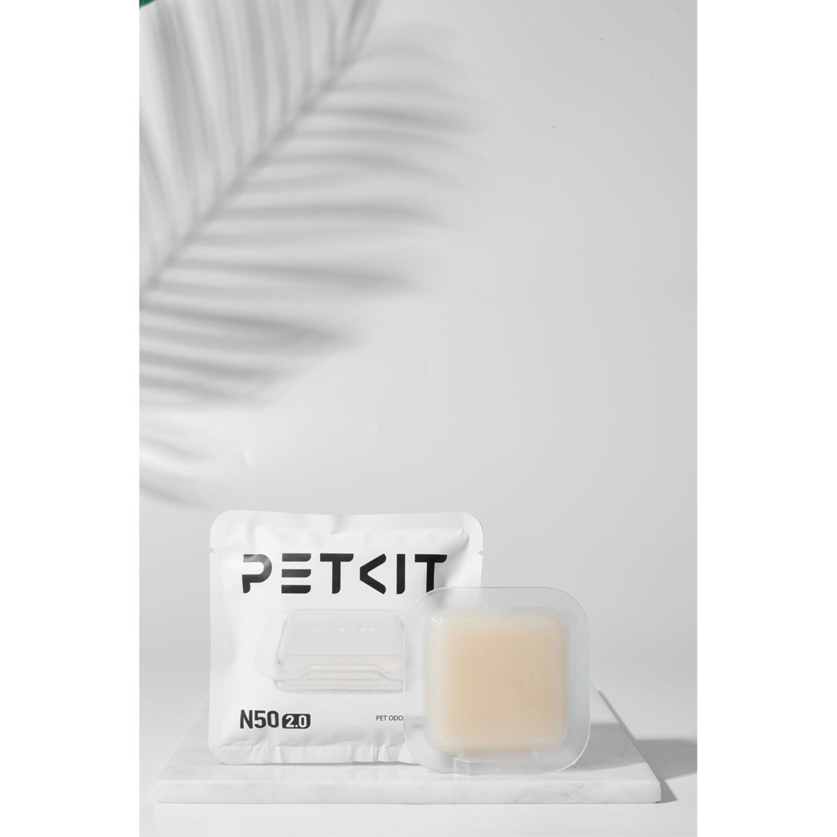 PETKIT-Produktverpackung und ein kleines transparentes Pad auf Marmor. Weißer Hintergrund mit Pflanzenschatten.