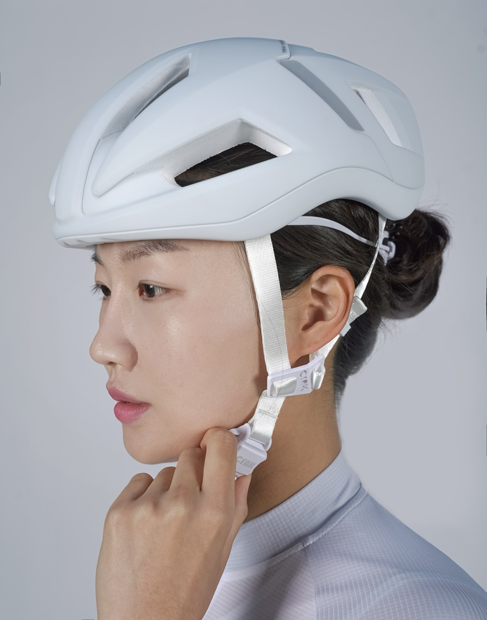 Eine Person trägt einen weißen Fahrradhelm mit Riemen und seitlichen Verstellmöglichkeiten.