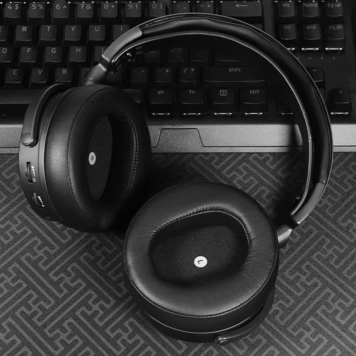 Czarne słuchawki na wzorzystej powierzchni, w pobliżu klawiatury. Słuchawki są skóropodobne.