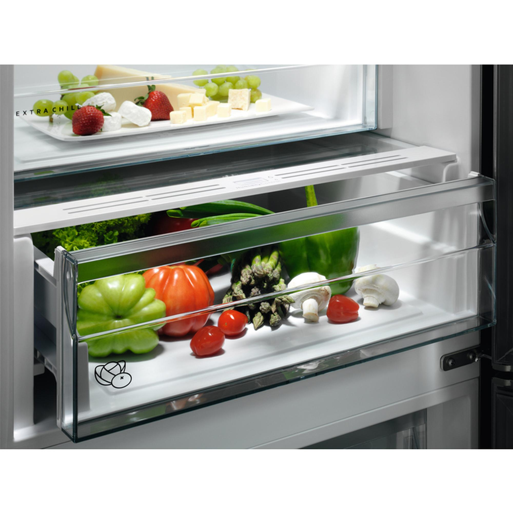 Interior de refrigerador con verduras, queso y fruta en cajones y estantes.