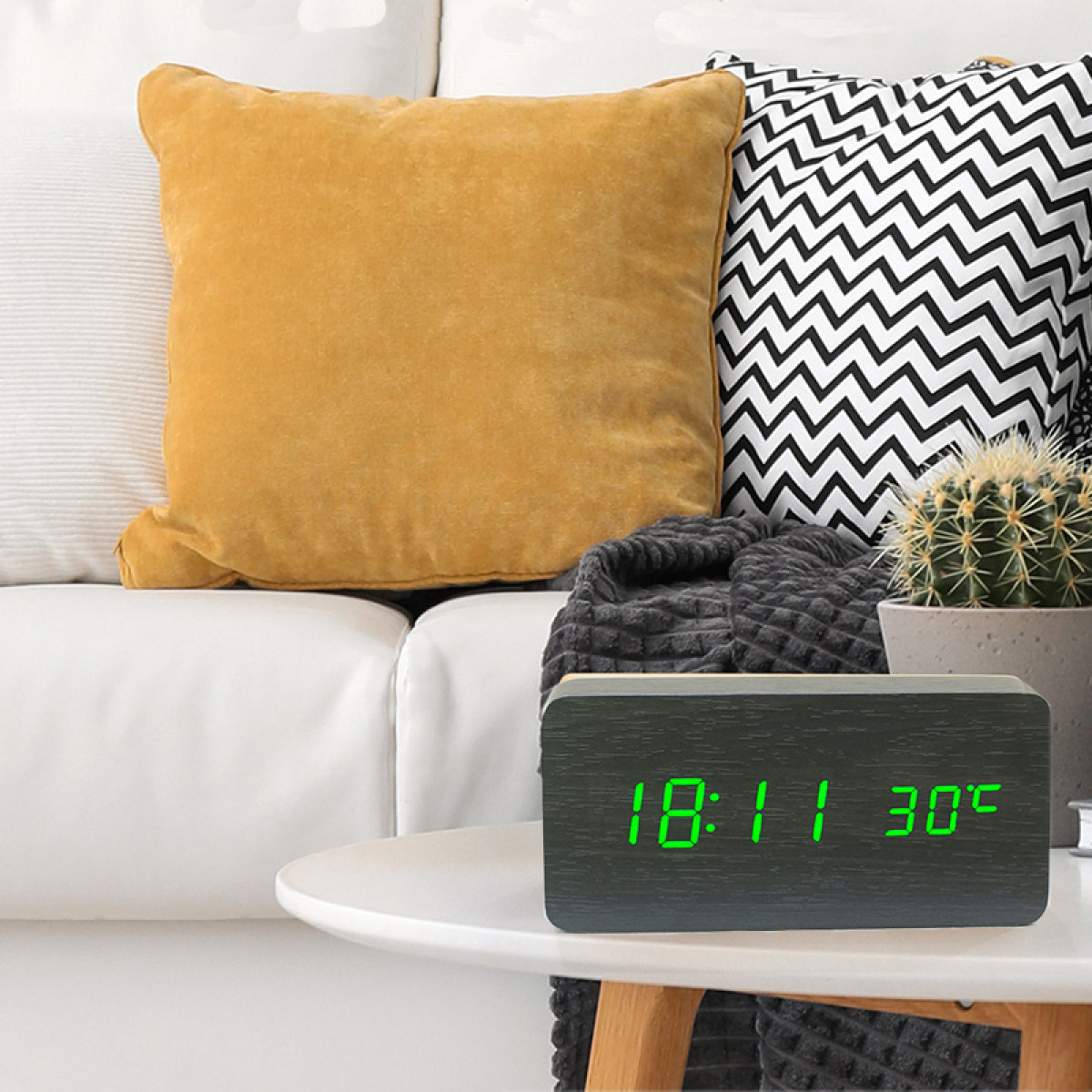 Drewniany zegar wyświetla godzinę i temperaturę na stole. W tle kanapa z poduszkami.