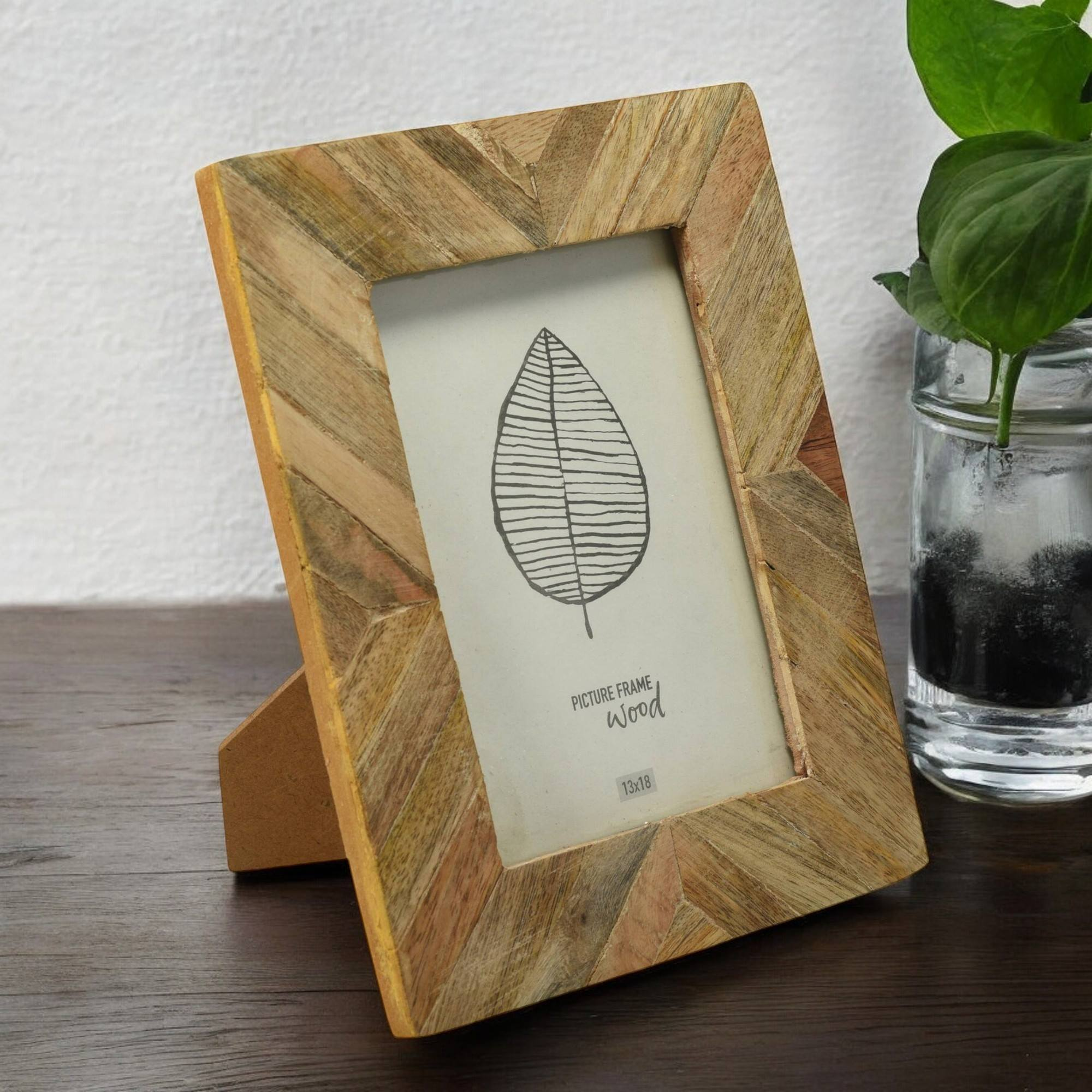 Un marco de fotos de madera, con un dibujo de hoja, apoyado sobre una superficie de madera junto a una planta.