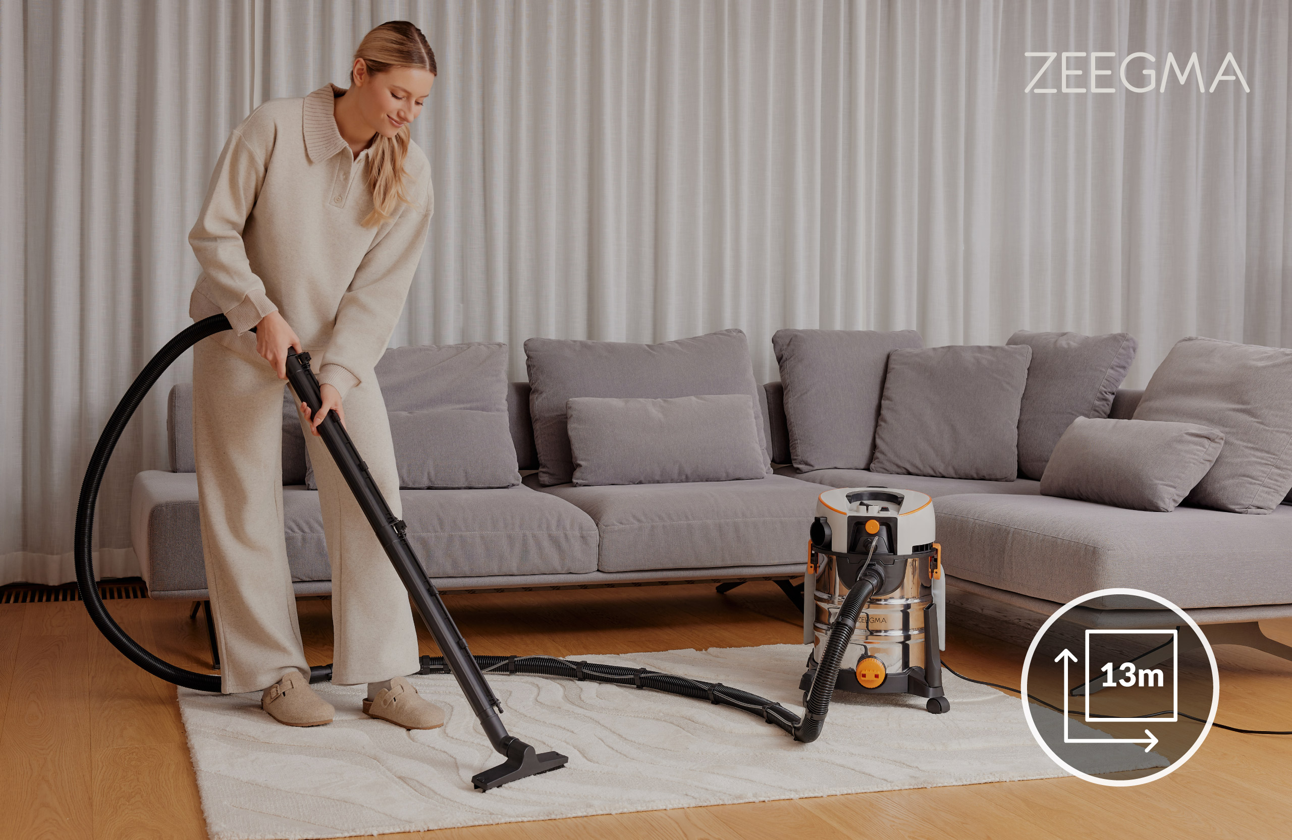 Kobieta odkurzająca dywan odkurzaczem Zeegma, szara sofa w tle.