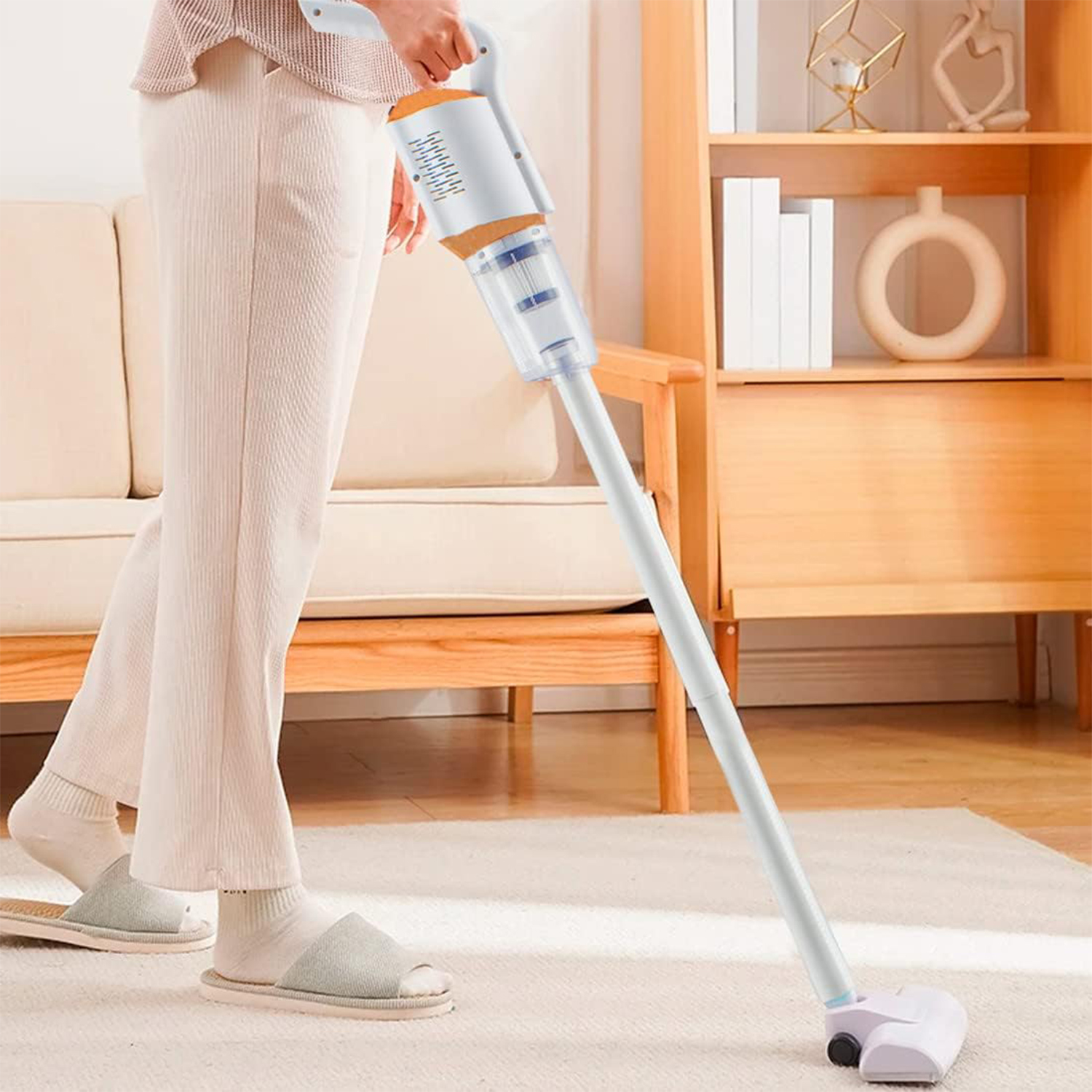 Una persona aspira una alfombra con una aspiradora inalámbrica blanca y naranja en una sala de estar.