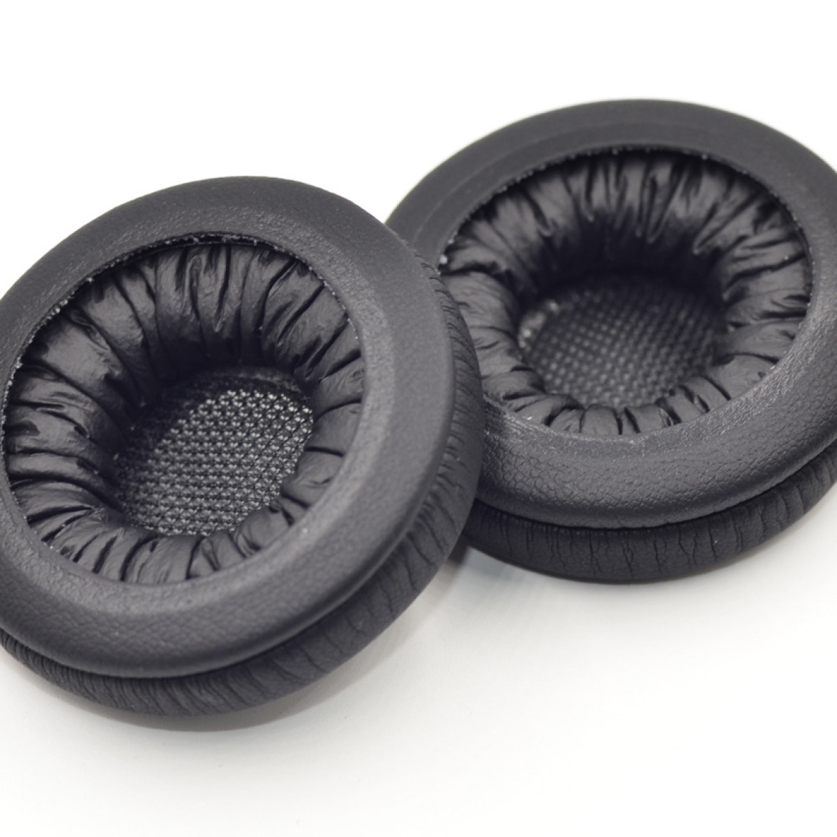 Dwie czarne, okrągłe poduszki do słuchawek. Wykonane są z miękkiego materiału i leżą na białej powierzchni.