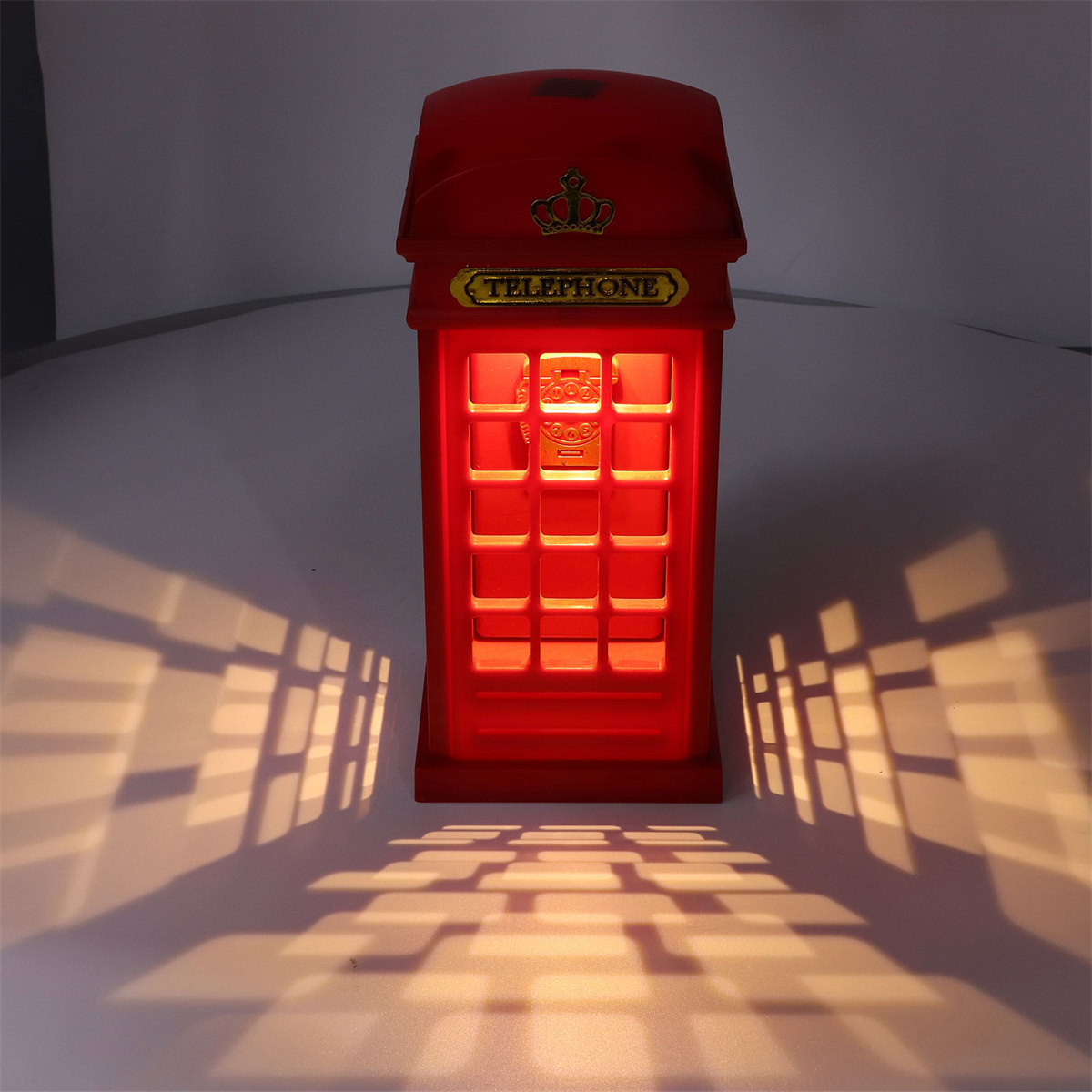 Eine rote Telefonzellenlampe wirft Schatten. Es hat eine goldene Krone und ein glühendes Innere.