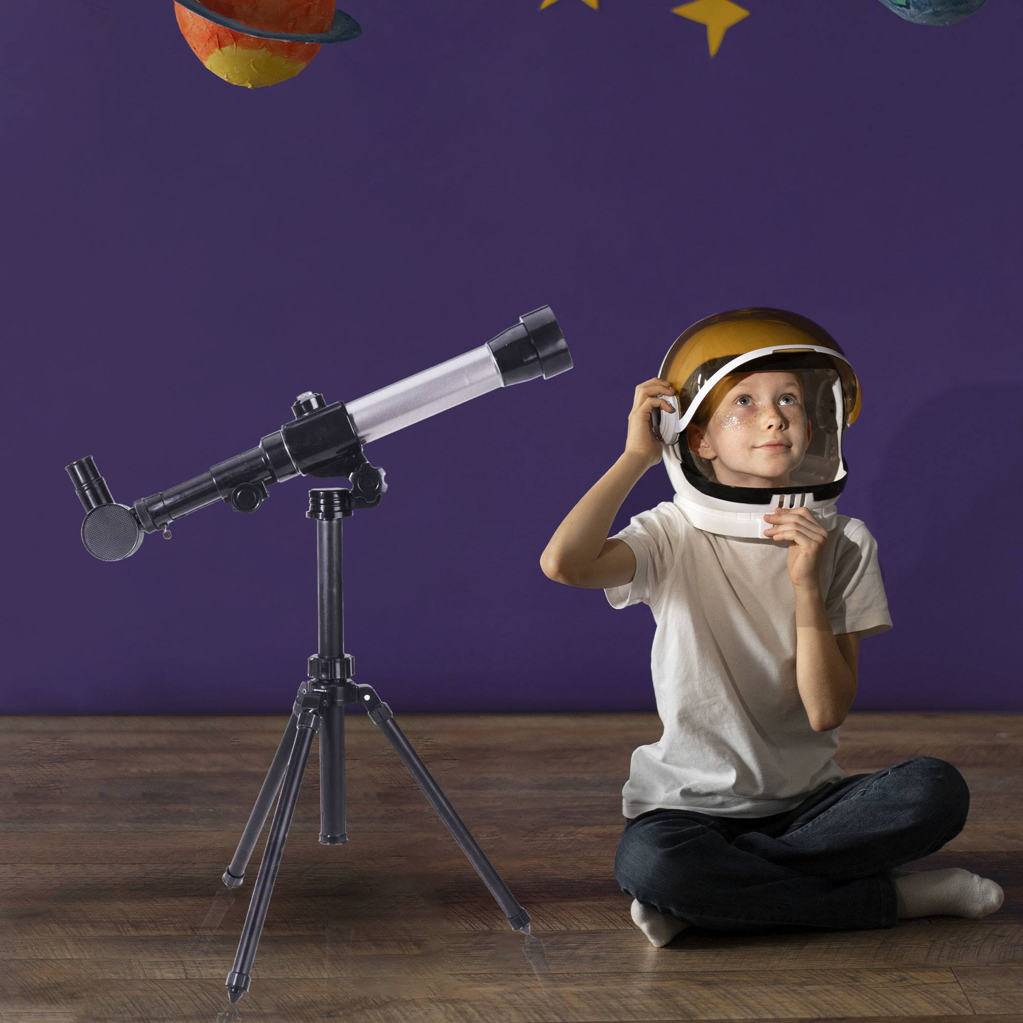 Niño pequeño con casco de astronauta mirando hacia arriba a planetas y estrellas. Telescopio al frente.