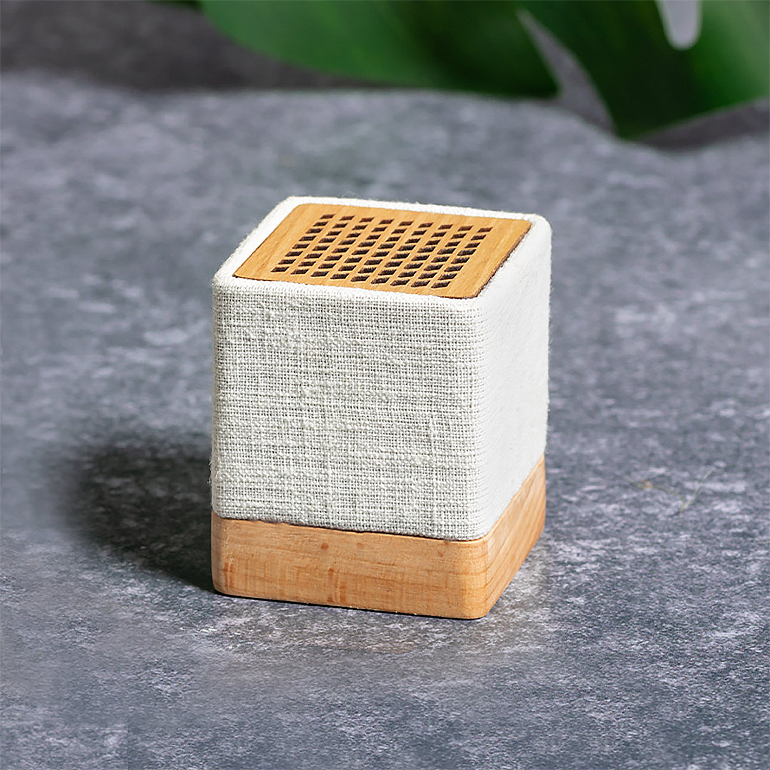 Un piccolo altoparlante a forma di cubo fatto di legno, tessuto e una griglia di legno sulla parte superiore, su una superficie grigia.