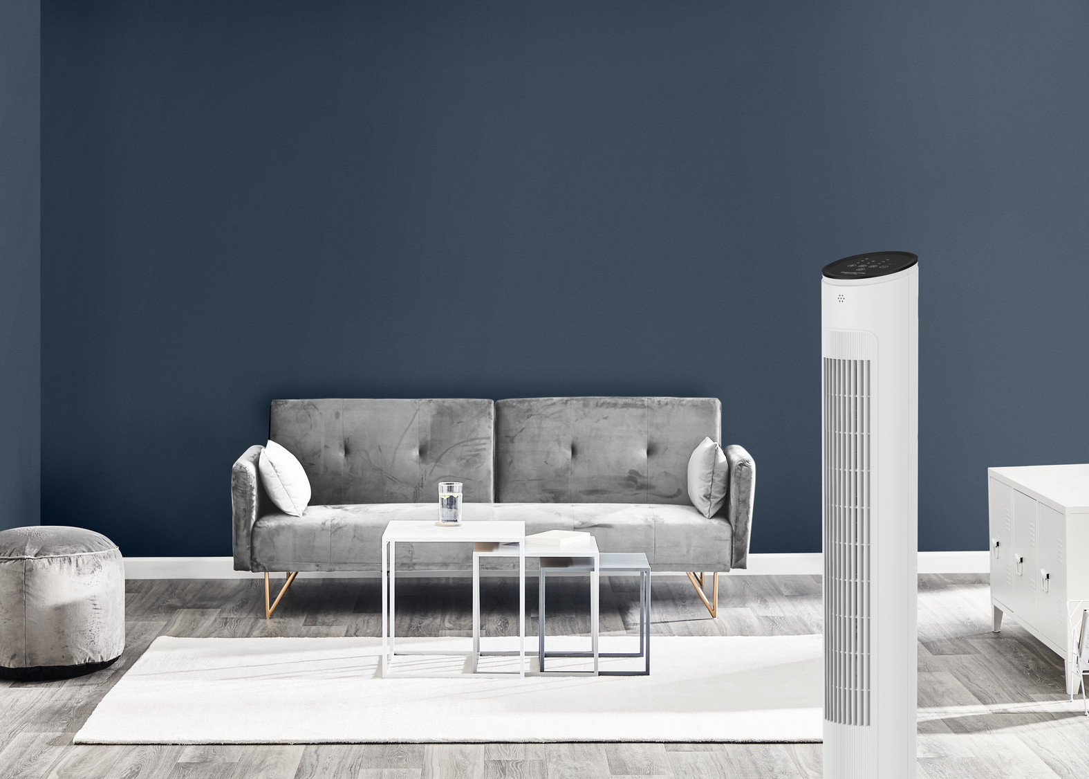 Salon z szarą sofą, białymi stolikami i białym wentylatorem. Niebieskie tło ściany.