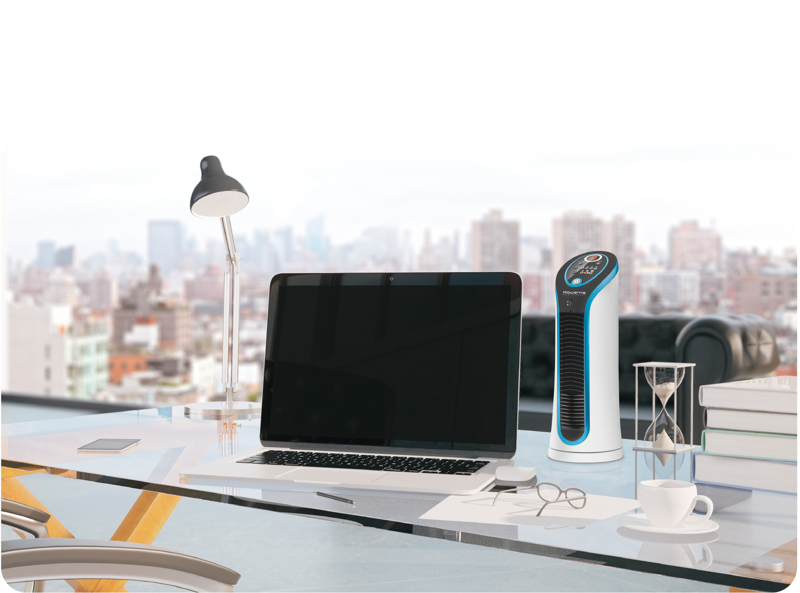Biurko z laptopem, lampą, oczyszczaczem powietrza i innymi przedmiotami. Przez okno widać panoramę miasta.