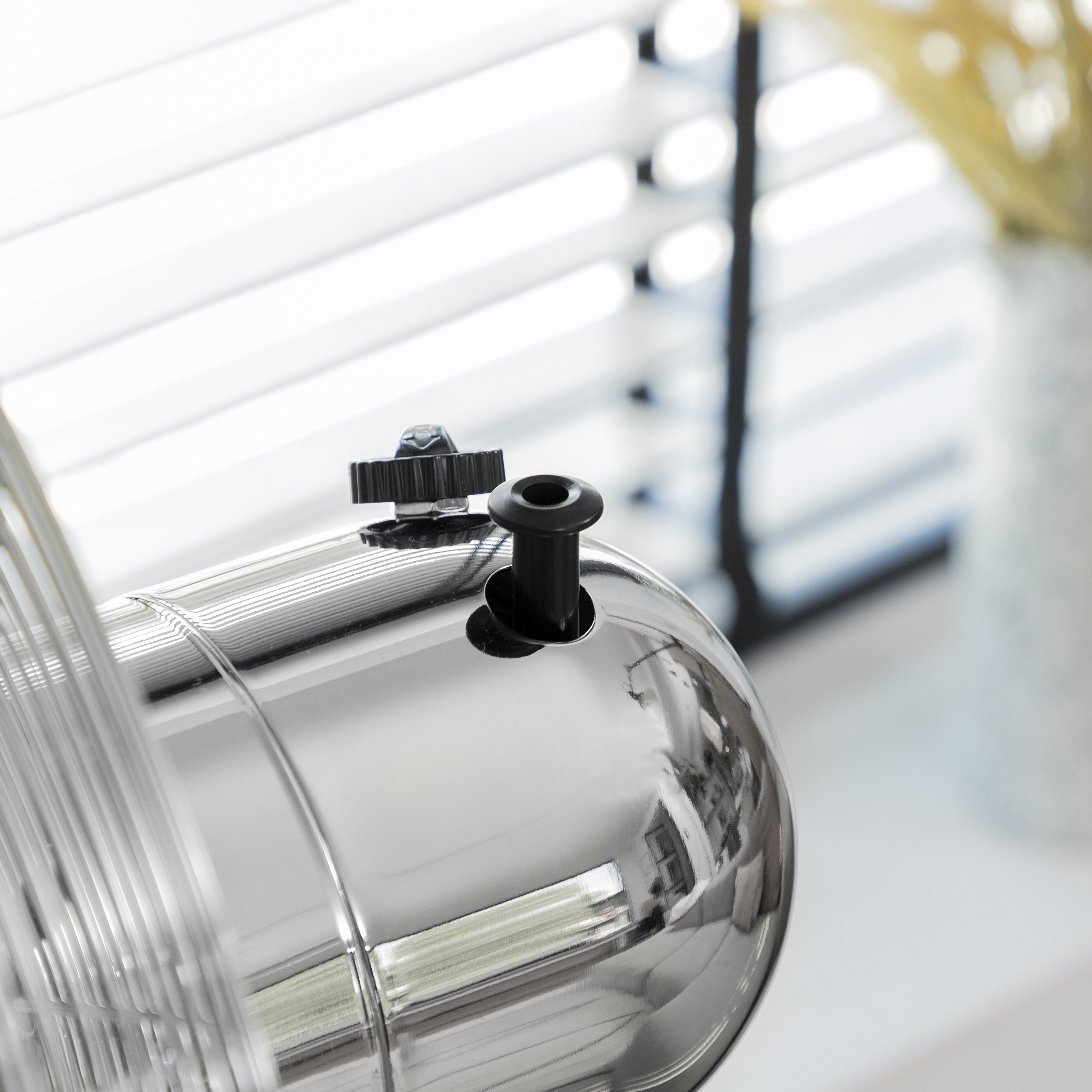Primo piano di un ventilatore cromato, che mostra il motore e la manopola di regolazione.