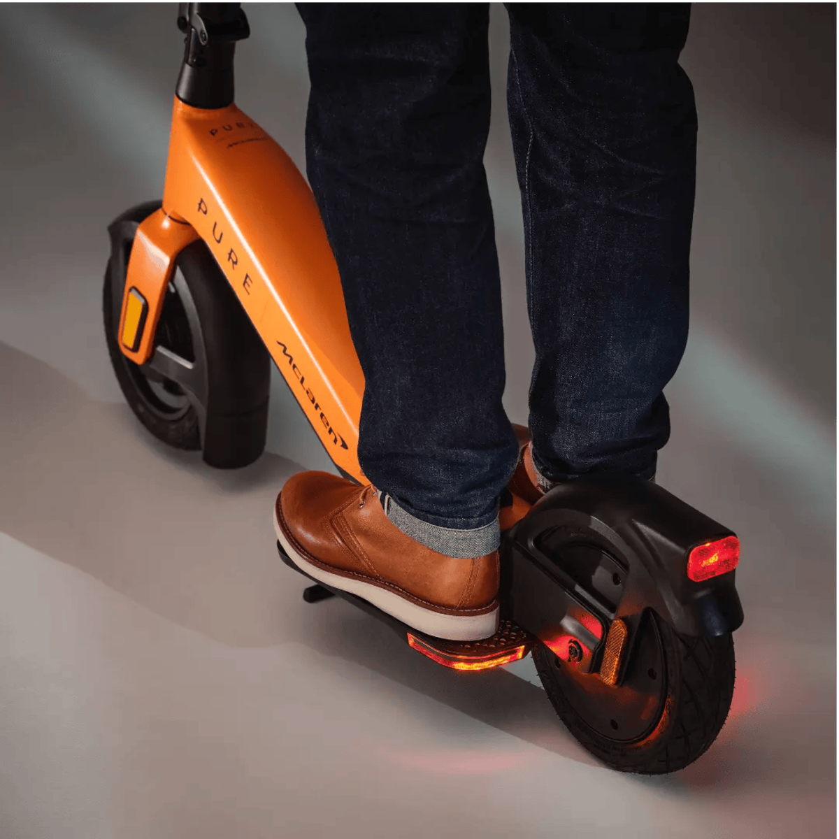 Orangener und schwarzer Elektroroller mit einer Person, die ihn fährt. Das Wort 'PURE' ist sichtbar.