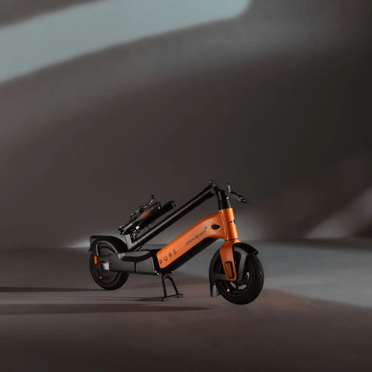 Ein orangefarbener und schwarzer Elektroroller mit 'McLaren' darauf, der auf einer grauen Oberfläche steht. Dunkler Hintergrund.