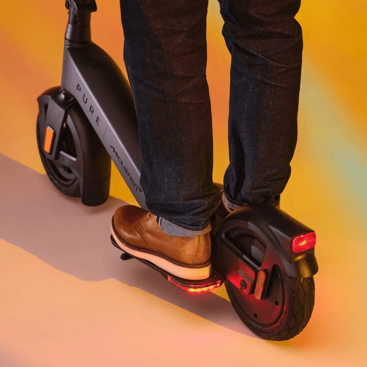 Person fährt einen schwarz-grauen Elektroroller, Beine und Füße sichtbar.