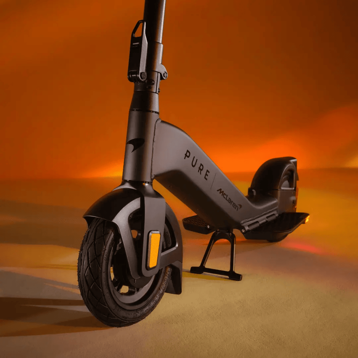 Ein schwarzer McLaren Pure Elektroroller vor einem orangefarbenen Hintergrund. Er hat einen schwarzen Reifen und Ständer.