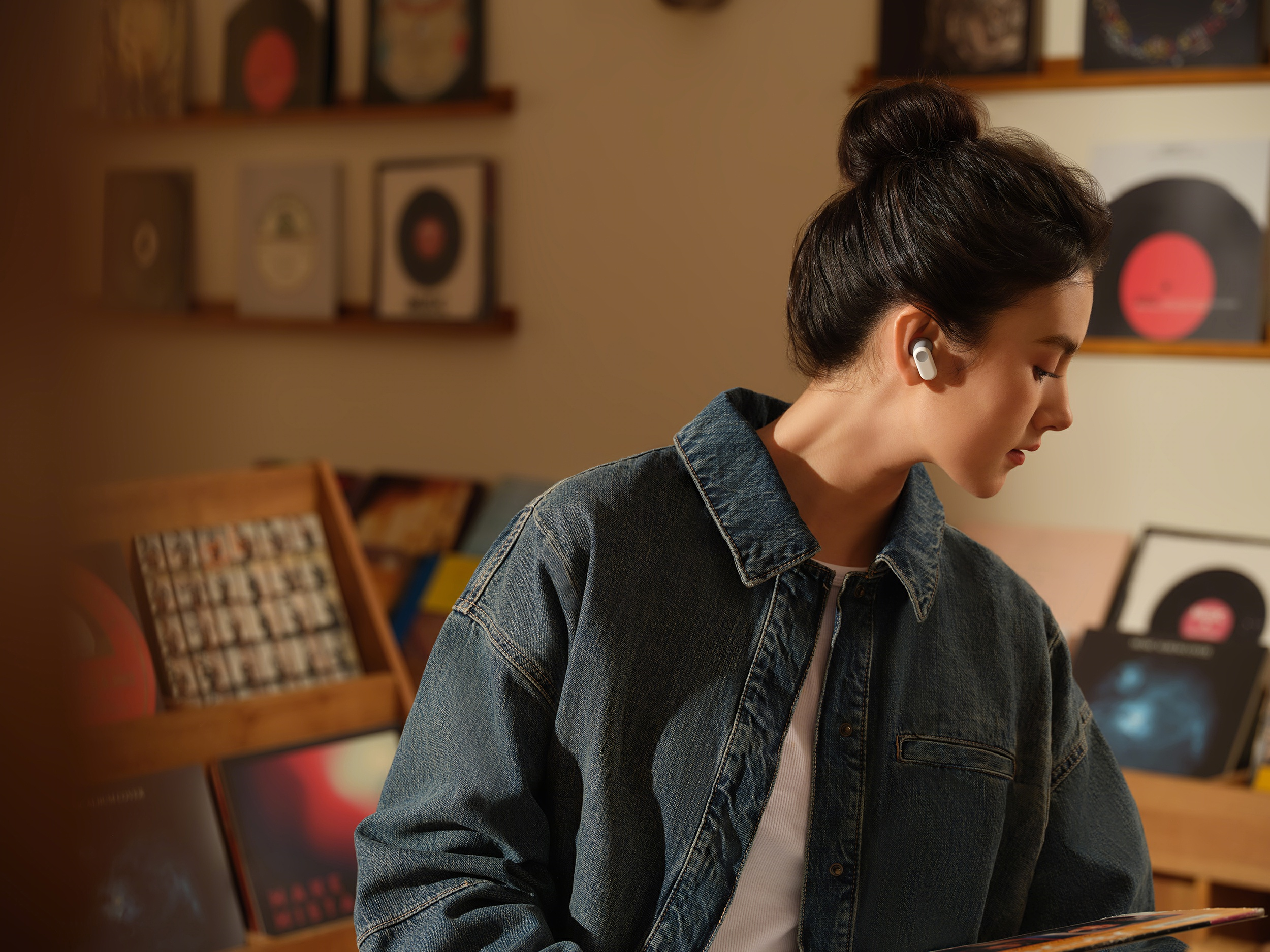 Una mujer con auriculares, chaqueta vaquera, en habitación con discos de vinilo.