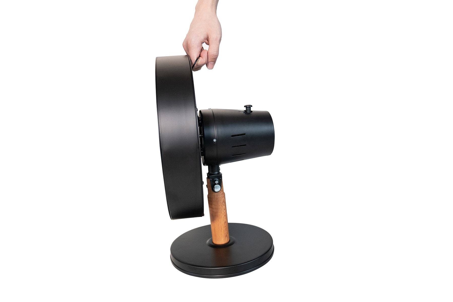 Ręka trzymająca czarny wentylator z drewnianą podstawą na białym tle. Wentylator jest w widoku z boku.