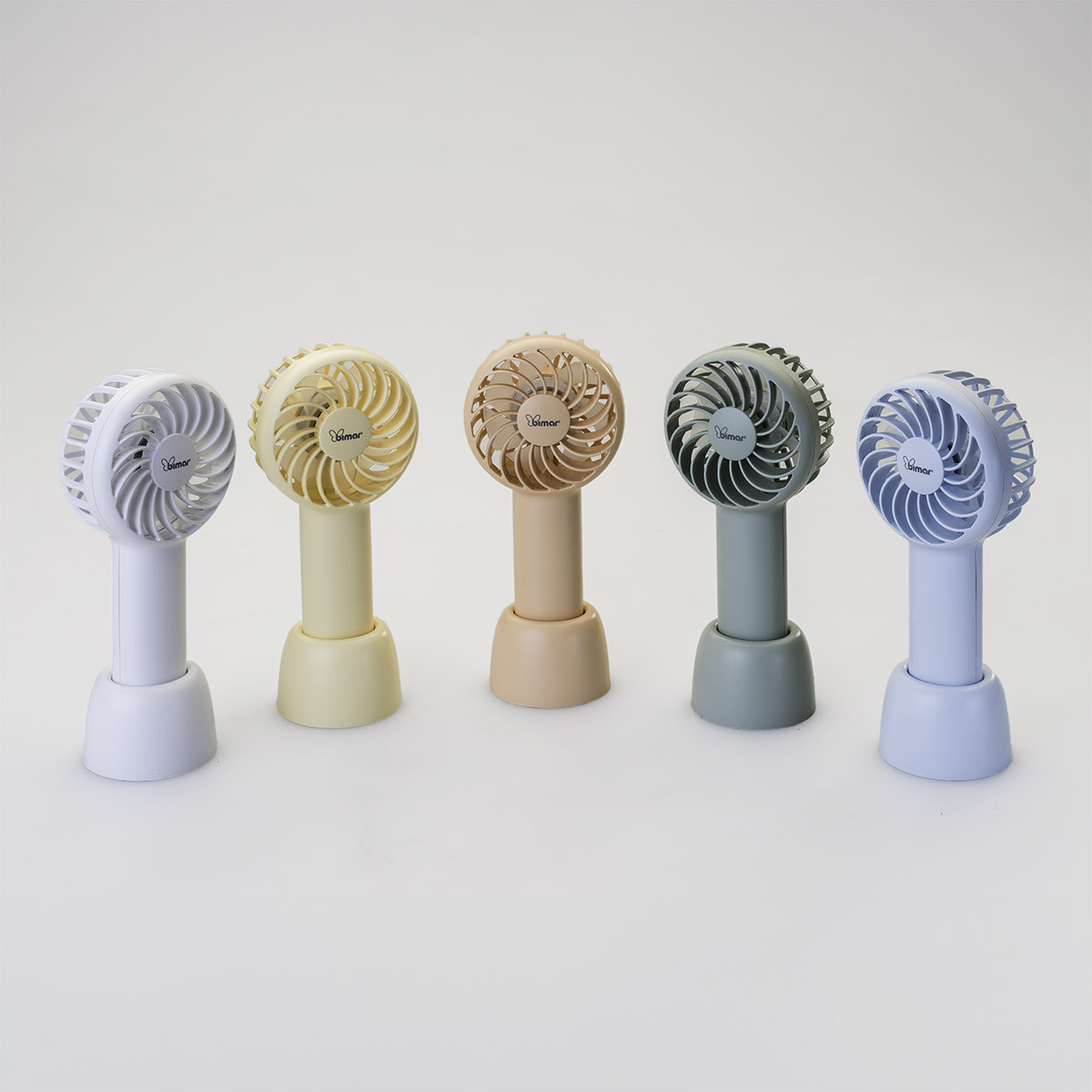 Cinque piccoli ventilatori portatili di diversi colori. Lo sfondo è bianco.
