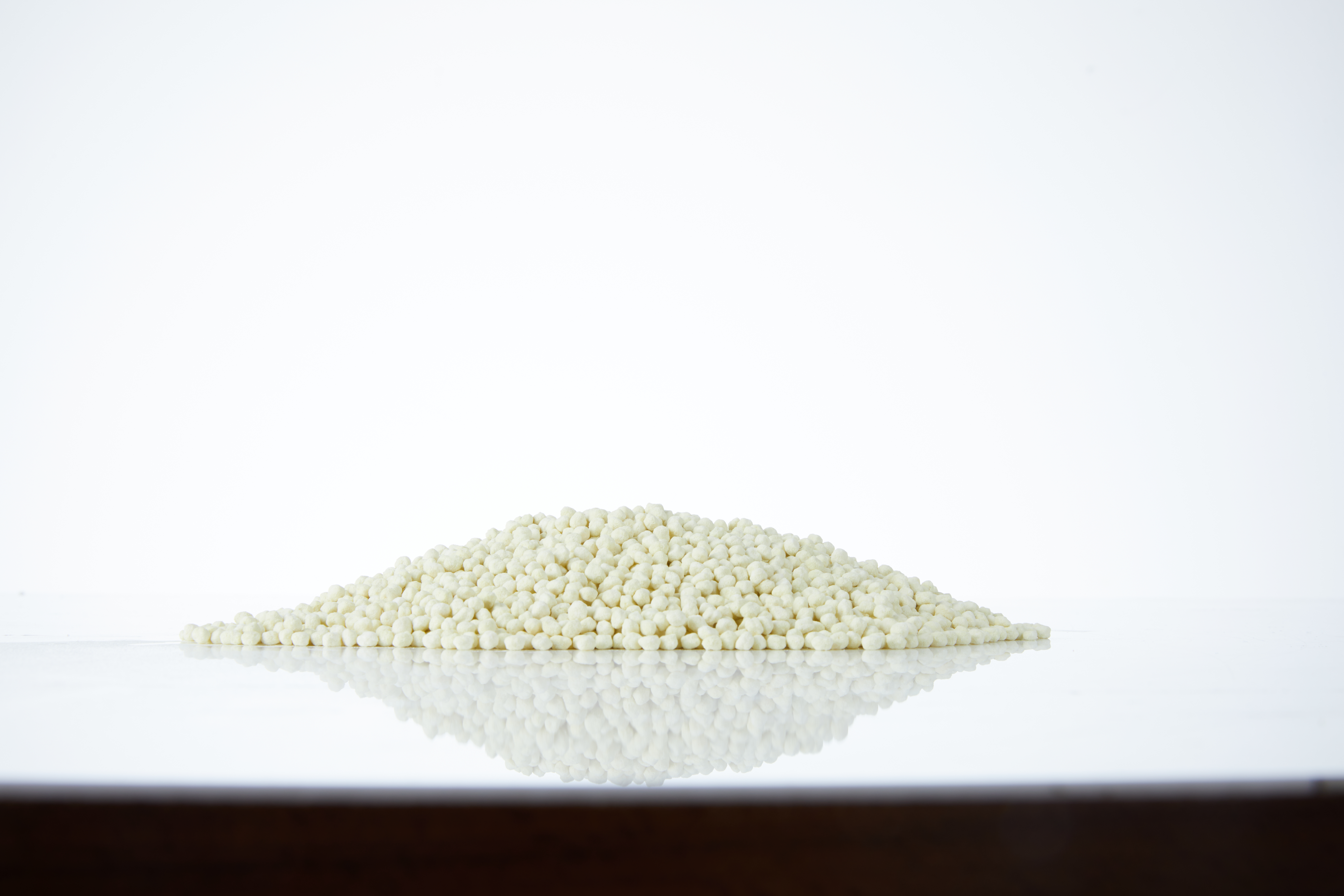 Yansıtıcı bir yüzey üzerinde, beyaz bir arka plan önünde küçük, beyazımsı toplar yığını.