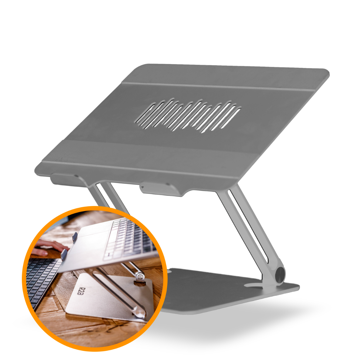 Grijze laptopstandaard. Verstelbaar, met een laptop. Houten tafel met toetsenbord op de achtergrond.