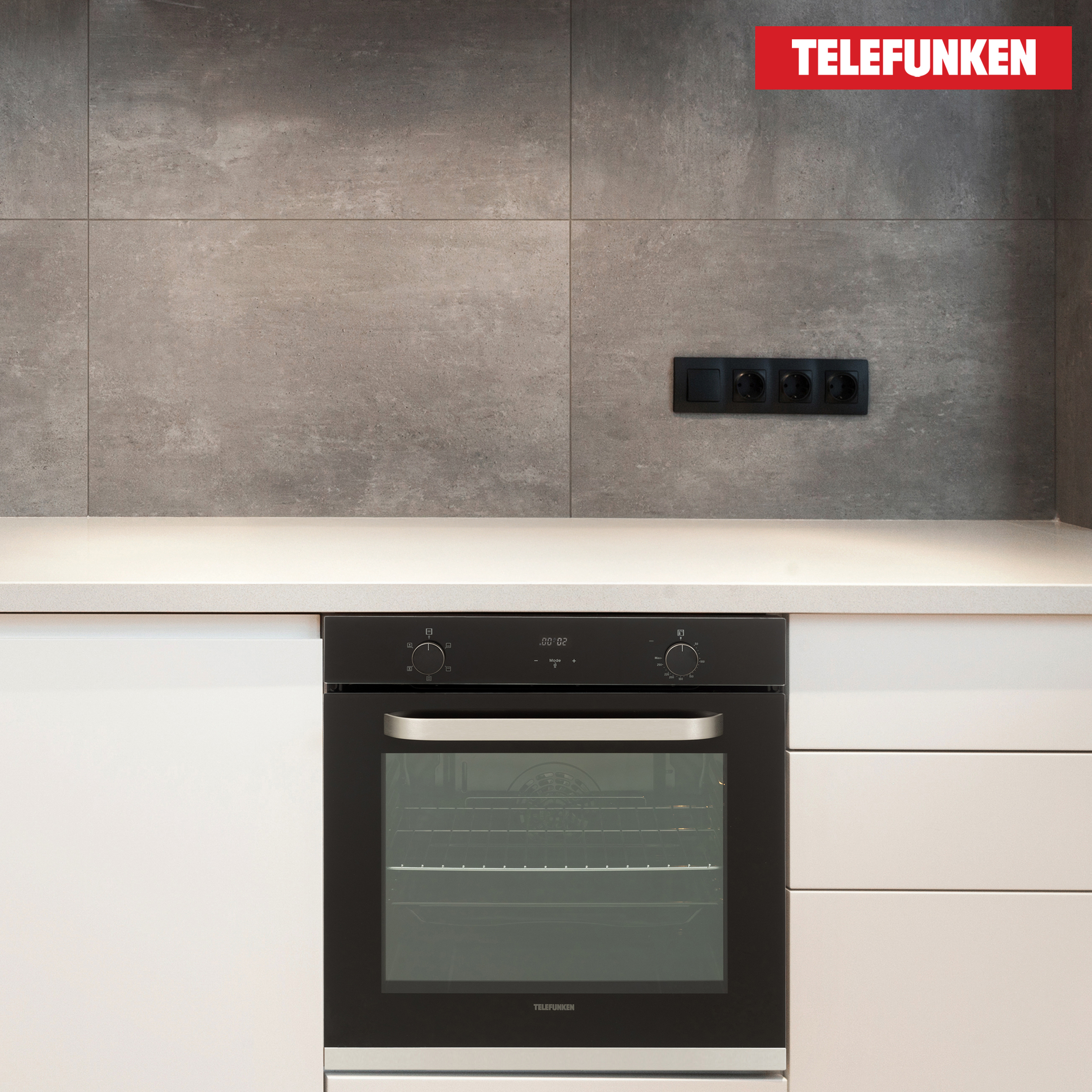 Ein schwarzer Ofen unter einer weißen Arbeitsplatte und drei Steckdosen, mit einem Telefunken-Logo.