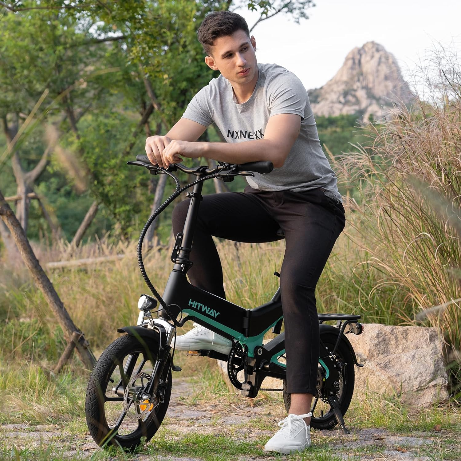 Ein Mann sitzt draußen auf einem schwarzen und türkisfarbenen Elektrofahrrad. Berg im Hintergrund.