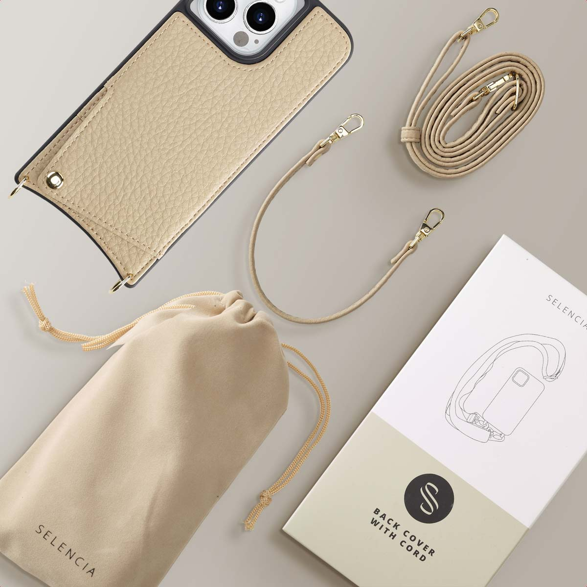 Telefoonhoes met riem, accessoires. Beige hoes, gouden details, trekkoordtas, witte doos, lichte achtergrond.