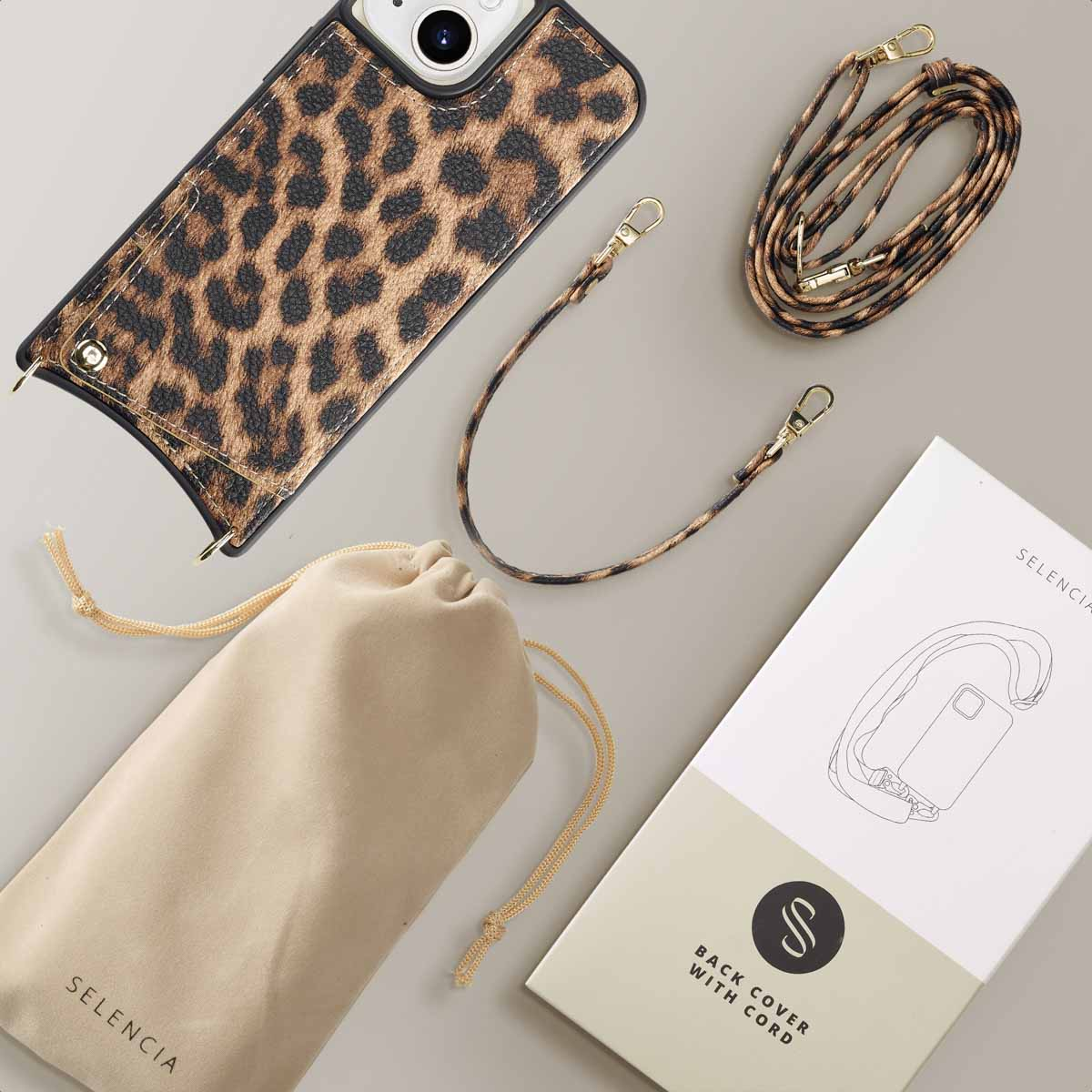 Een telefoonhoesje met luipaardprint en een bandje, liggend op een grijs oppervlak. Een tas en een doos ernaast.