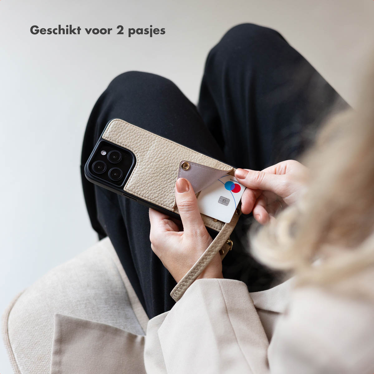 Le mani di una persona che tiene una custodia per telefono. Si sta inserendo una carta di credito. Sfondo beige.
