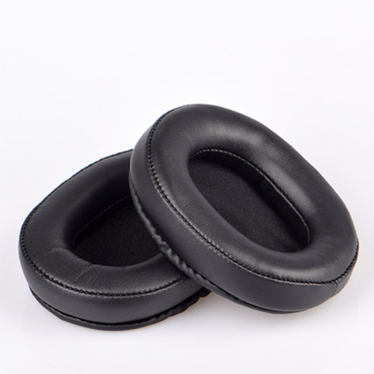 Dwie czarne, owalne poduszki do słuchawek, na białej powierzchni, ujęcie z bliska.