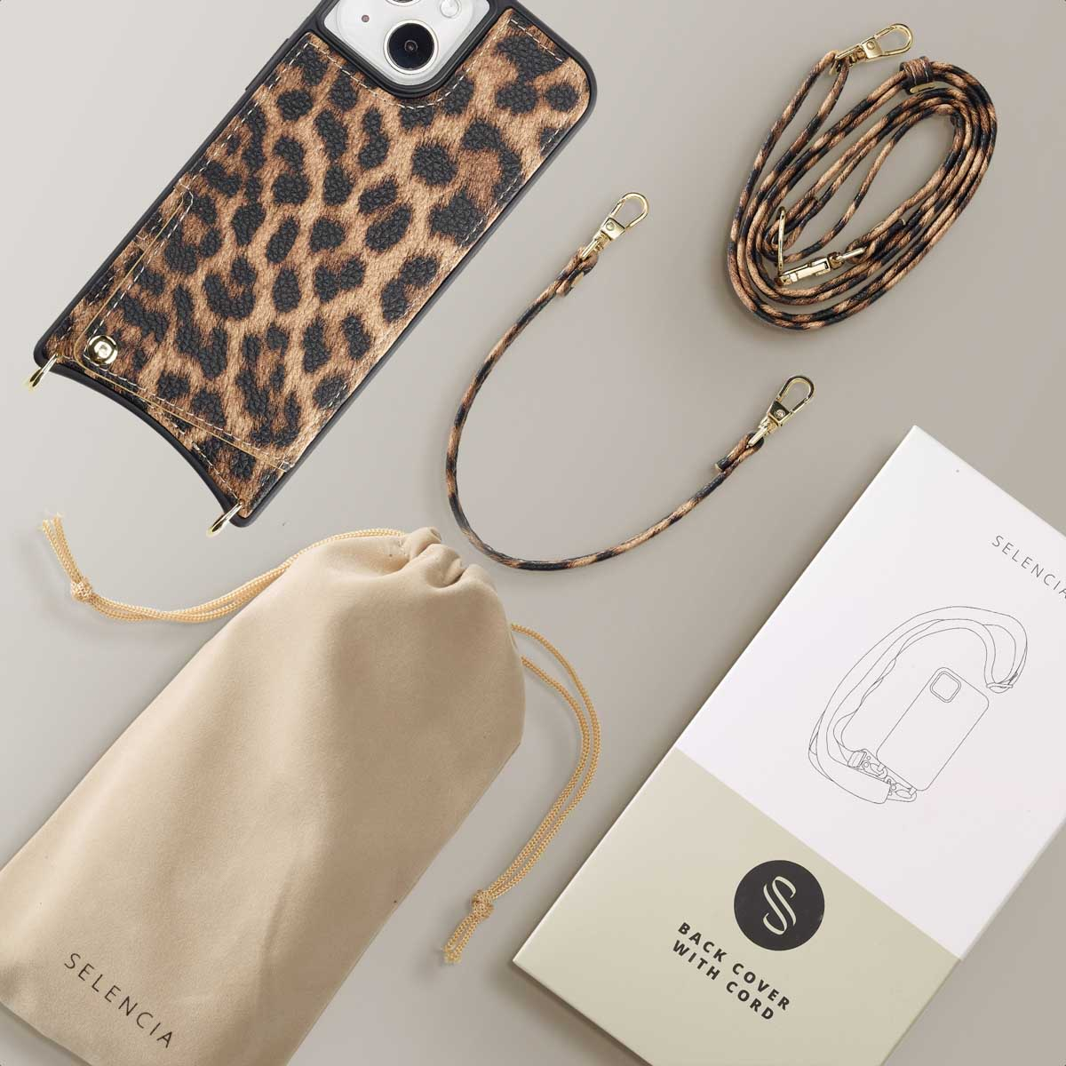Une coque de téléphone à imprimé léopard avec une sangle, un sac et un livret sur une surface grise.