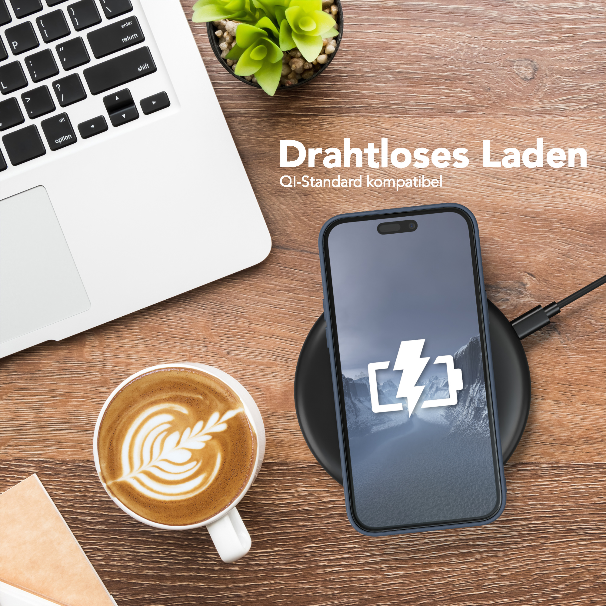 Telefon wird drahtlos auf einem Pad neben einem Laptop und einer Tasse Kaffee geladen.