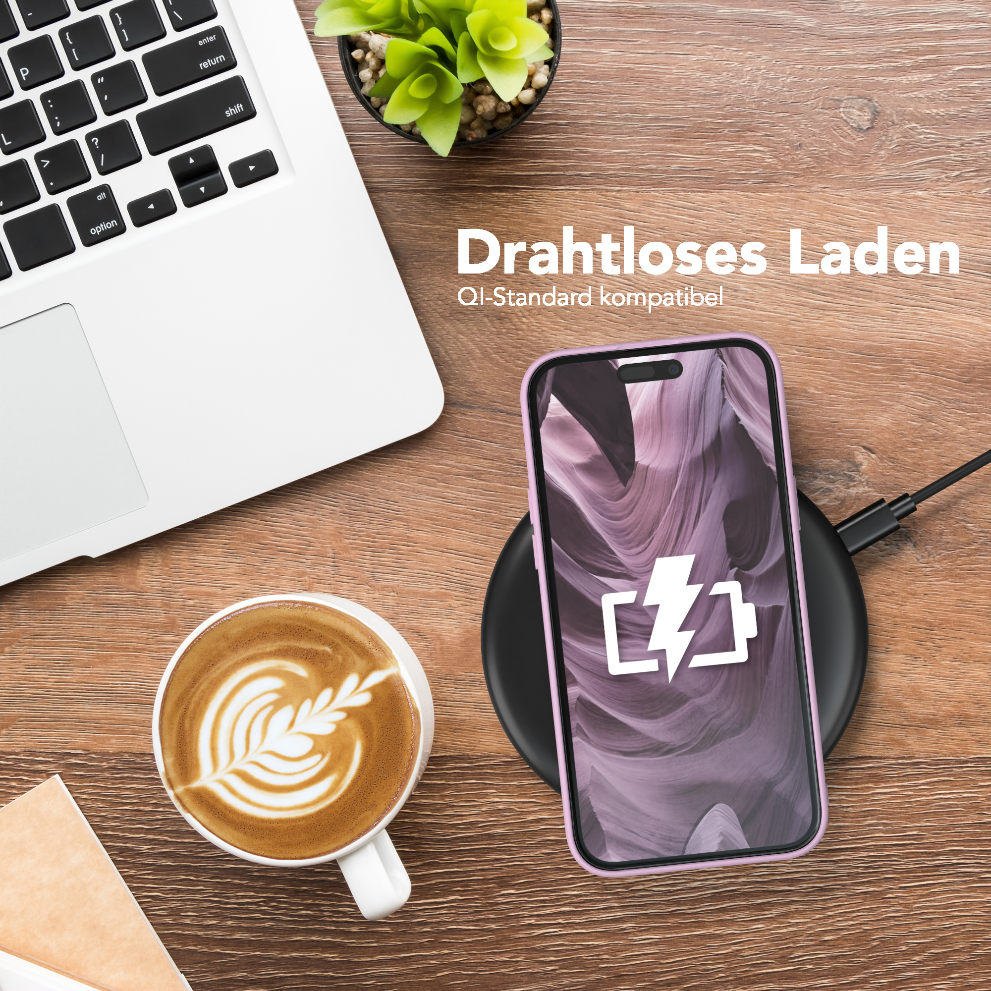 Telefon lädt auf schwarzem Pad, neben Laptop und Kaffee. Holzoberfläche mit Pflanze im Hintergrund.