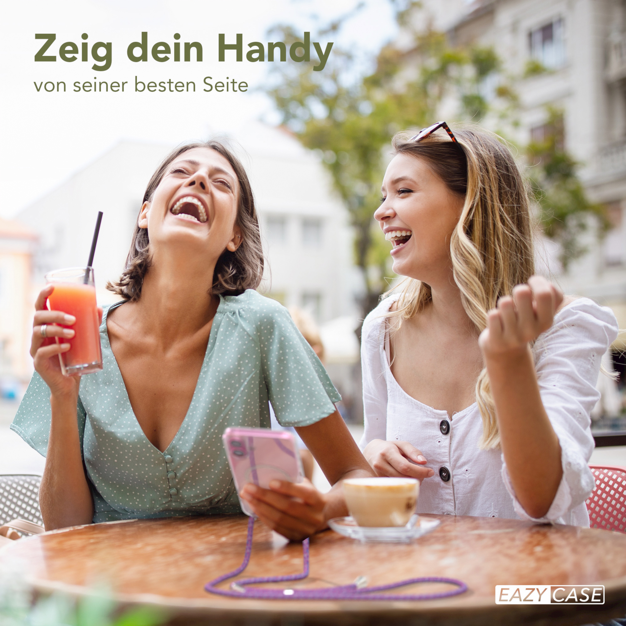 Zwei lachende Frauen schauen auf ein Handy. Eine hält Getränk, die andere Kaffee.